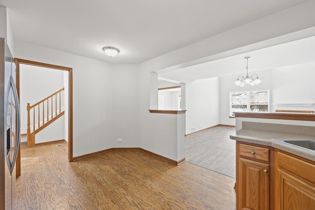 interior space featuring light wood-type flooring, a chandelier, stainless steel fridge, and hanging light fixtures