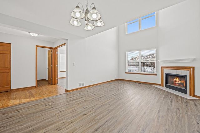 unfurnished living room with light wood-type flooring, a tiled fireplace, and a notable chandelier