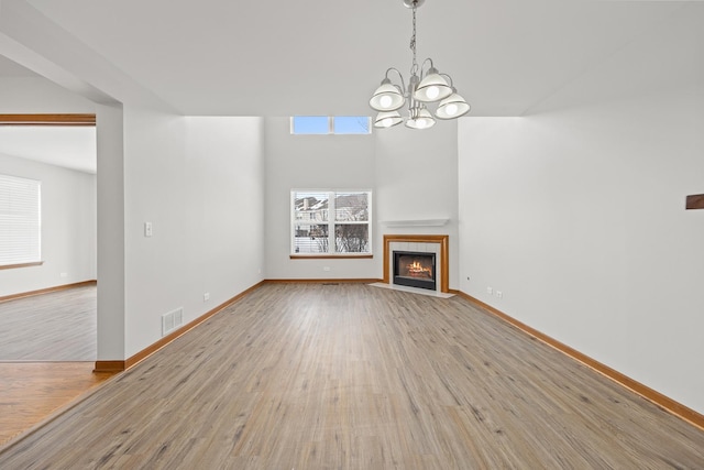 unfurnished living room featuring an inviting chandelier, light hardwood / wood-style floors, and a tiled fireplace