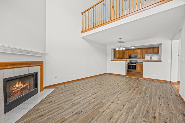 unfurnished living room featuring a fireplace, light hardwood / wood-style floors, a chandelier, and a towering ceiling