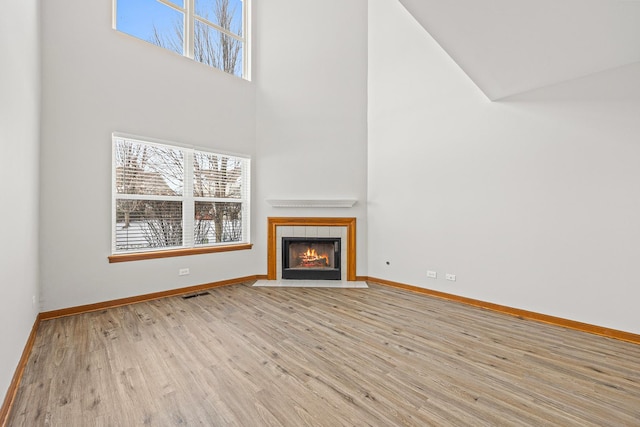 unfurnished living room with light wood-type flooring, a high ceiling, a fireplace, and plenty of natural light