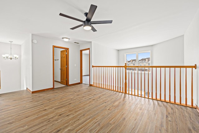 unfurnished room with ceiling fan with notable chandelier and light hardwood / wood-style floors