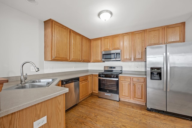 kitchen with sink, light wood-type flooring, stainless steel appliances, and decorative backsplash