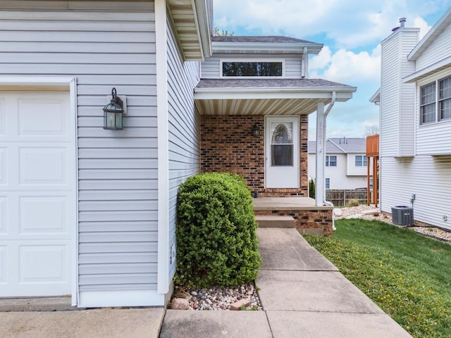 view of exterior entry with roof with shingles, a garage, central air condition unit, brick siding, and a yard