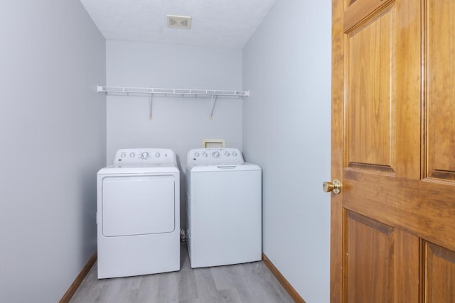 clothes washing area with baseboards, laundry area, washer and clothes dryer, and light wood-type flooring