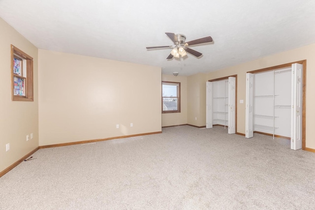 unfurnished bedroom featuring baseboards, a ceiling fan, multiple closets, and light carpet