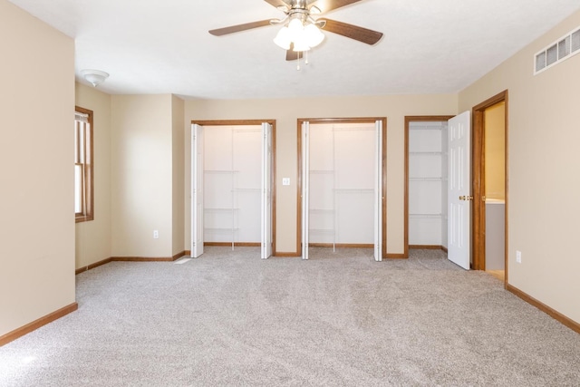 unfurnished bedroom with baseboards, two closets, carpet flooring, and visible vents