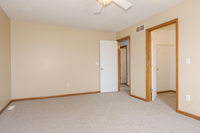 unfurnished bedroom featuring a walk in closet, baseboards, light carpet, and visible vents