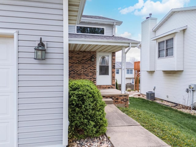 doorway to property featuring central AC, covered porch, brick siding, a shingled roof, and a lawn