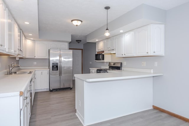 kitchen featuring appliances with stainless steel finishes, a sink, a peninsula, light wood-style floors, and white cabinetry