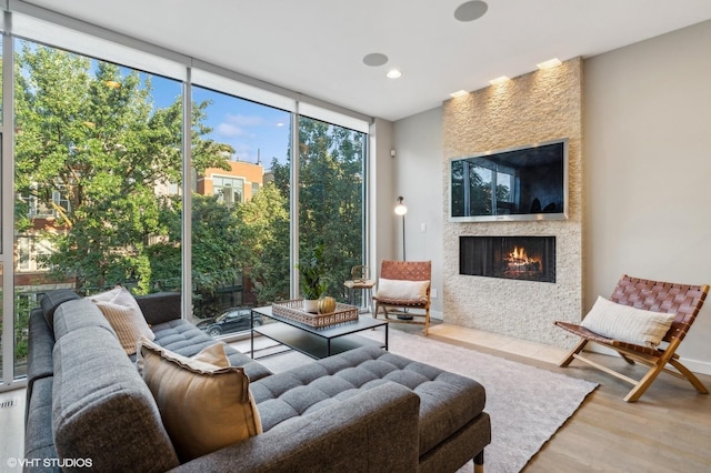 living room with hardwood / wood-style floors, a wall of windows, and a large fireplace