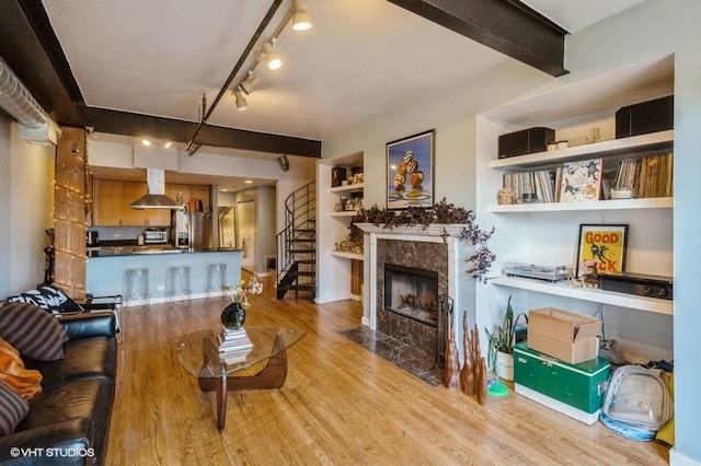 living room featuring rail lighting, light hardwood / wood-style flooring, built in features, beamed ceiling, and a high end fireplace