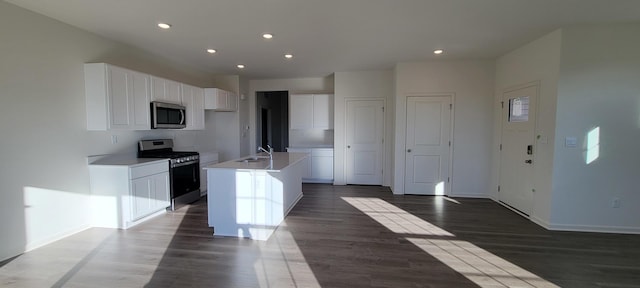 kitchen with a kitchen island with sink, dark wood-type flooring, stainless steel appliances, and white cabinets