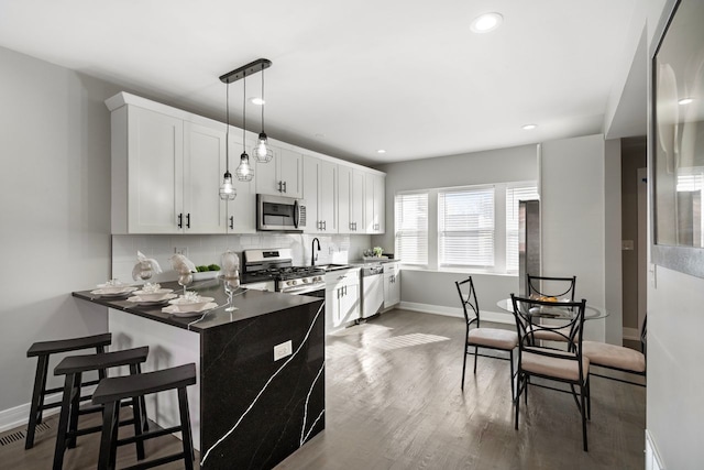 kitchen with pendant lighting, sink, white cabinets, decorative backsplash, and stainless steel appliances