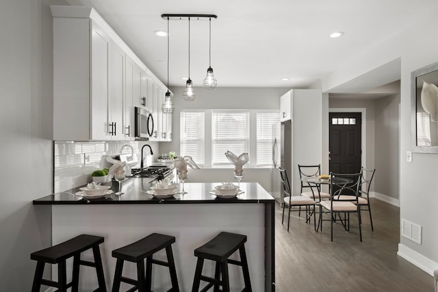 kitchen featuring decorative light fixtures, kitchen peninsula, white cabinets, stainless steel appliances, and backsplash