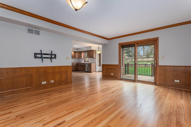 unfurnished living room with light wood finished floors, a wainscoted wall, and visible vents