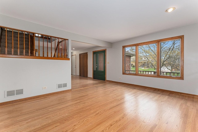 unfurnished room featuring stairs, visible vents, light wood-style floors, and baseboards