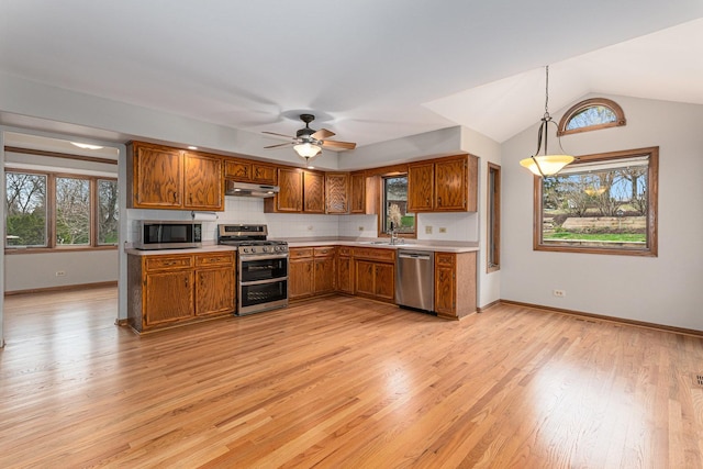 kitchen with stainless steel appliances, light wood-style floors, under cabinet range hood, light countertops, and brown cabinets