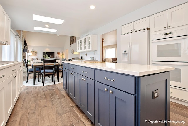 kitchen featuring white cabinetry, white appliances, light hardwood / wood-style flooring, and a kitchen island