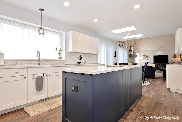 kitchen with decorative light fixtures, vaulted ceiling with skylight, a kitchen island, and white cabinets