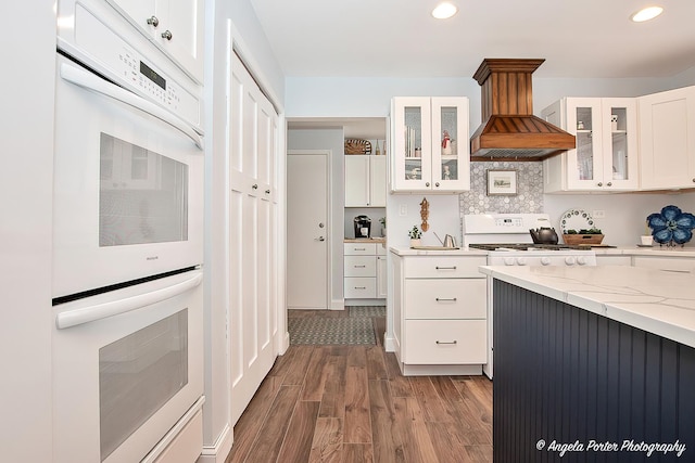 kitchen with range, white cabinetry, double oven, light stone counters, and custom range hood