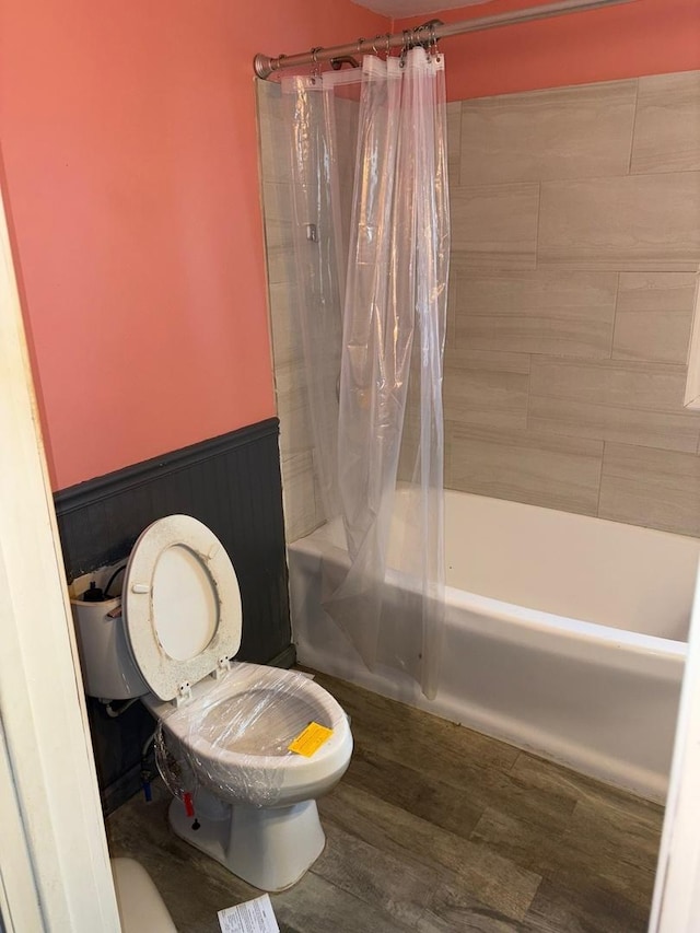 bathroom with wood-type flooring, shower / bath combination with curtain, and toilet