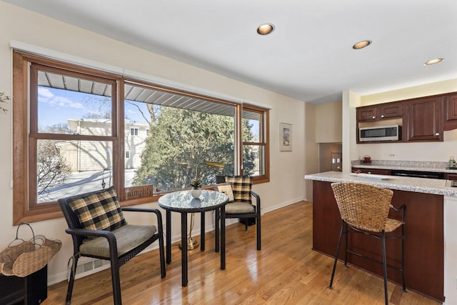 kitchen with dark brown cabinetry, recessed lighting, a kitchen breakfast bar, light wood-type flooring, and stainless steel microwave