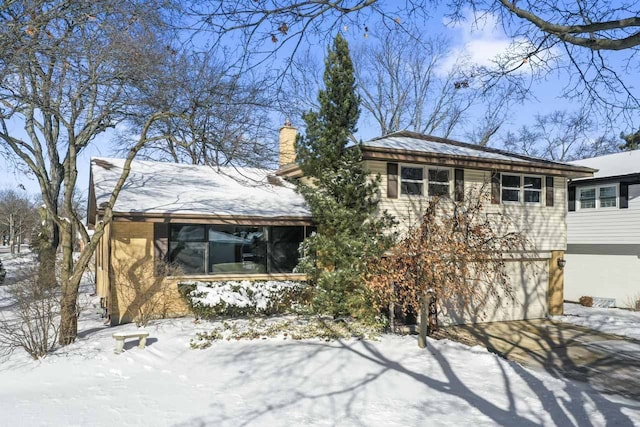 view of front of property with driveway, a sunroom, a garage, and a chimney