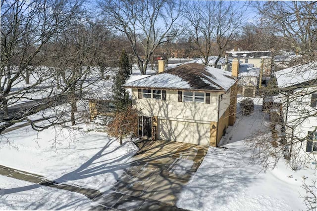 snow covered structure featuring driveway and an attached garage