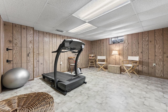 exercise area with a paneled ceiling, wooden walls, visible vents, and tile patterned floors