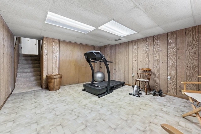 workout room with a paneled ceiling, wooden walls, visible vents, and tile patterned floors