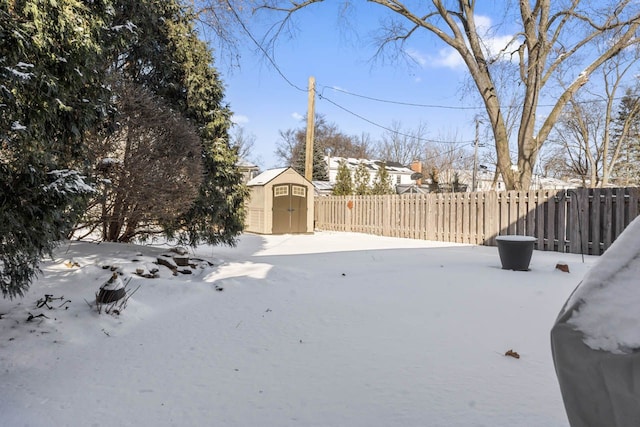 yard layered in snow with a storage shed, an outbuilding, and fence