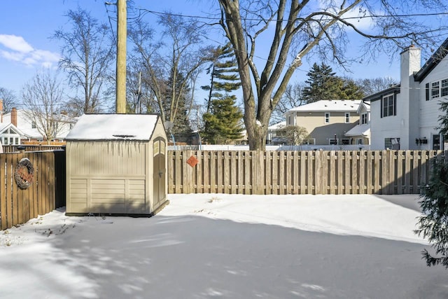 snow covered patio featuring a shed, a fenced backyard, and an outdoor structure