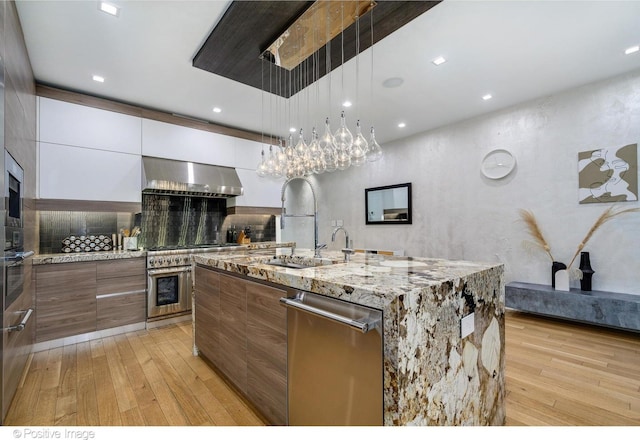 kitchen featuring a large island, wall chimney range hood, pendant lighting, sink, and white cabinets