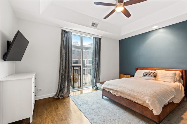 bedroom featuring a tray ceiling, dark wood-style flooring, visible vents, access to outside, and baseboards