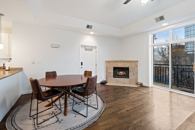 dining space with dark wood-style floors, a raised ceiling, visible vents, and a fireplace