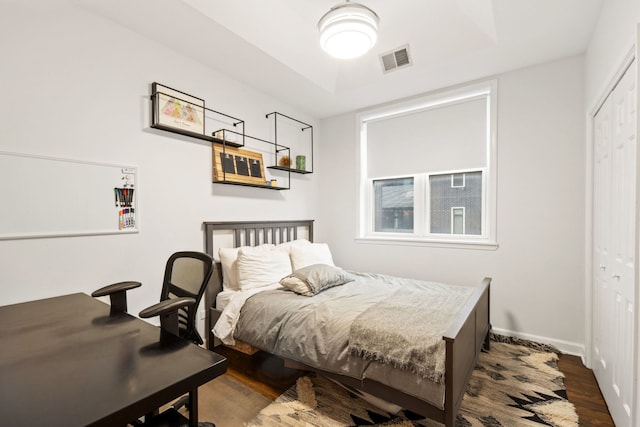 bedroom featuring baseboards, visible vents, a raised ceiling, wood finished floors, and a closet