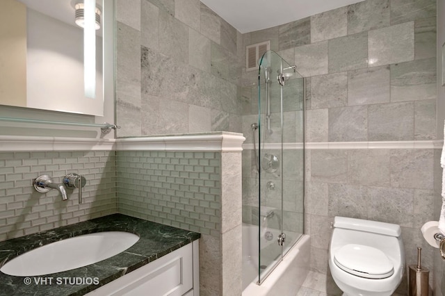 full bathroom with bath / shower combo with glass door, vanity, toilet, and tile walls