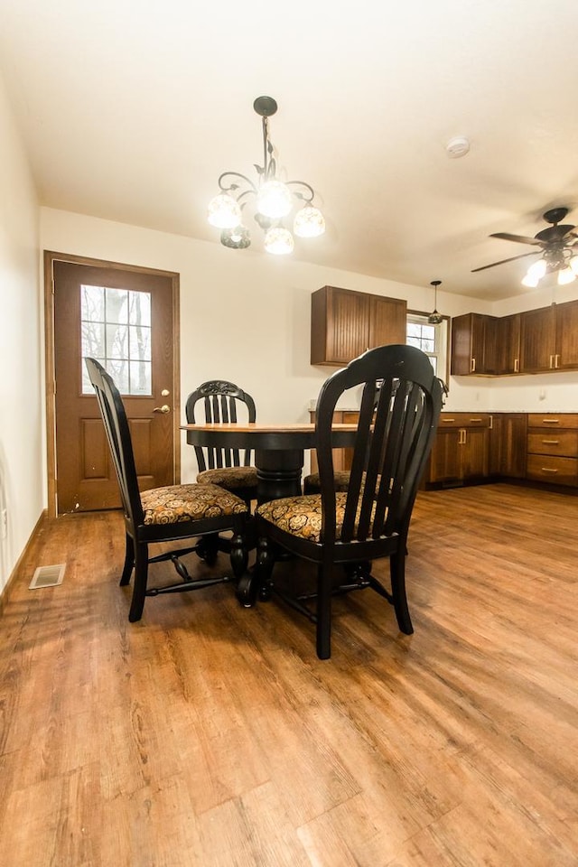 dining space with ceiling fan with notable chandelier, plenty of natural light, and light hardwood / wood-style floors