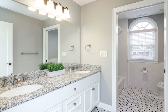 bathroom featuring toilet, double vanity, a sink, and tile patterned floors