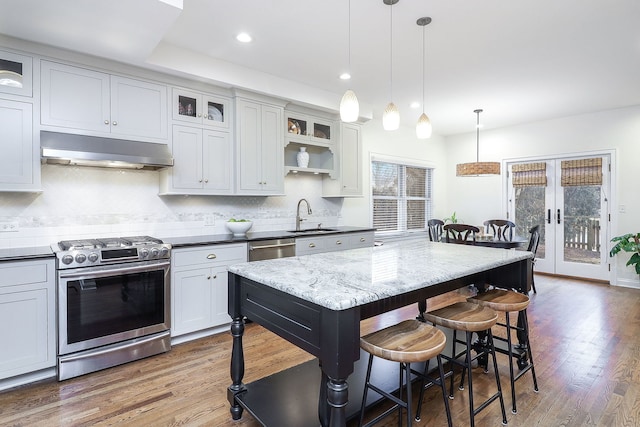 kitchen with decorative light fixtures, under cabinet range hood, a breakfast bar, appliances with stainless steel finishes, and glass insert cabinets