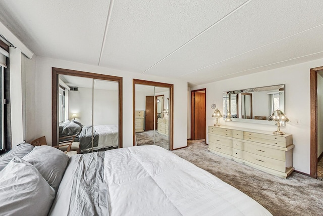 bedroom featuring a textured ceiling, multiple closets, and light colored carpet