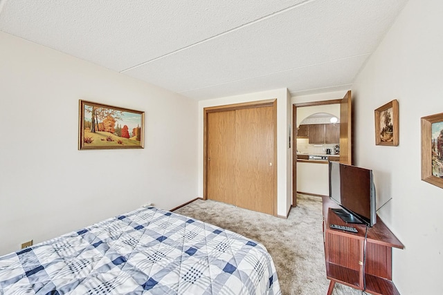 bedroom with a closet, baseboards, a textured ceiling, and light colored carpet