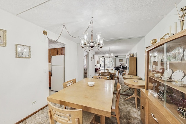 dining area with carpet, a textured ceiling, baseboards, and an inviting chandelier