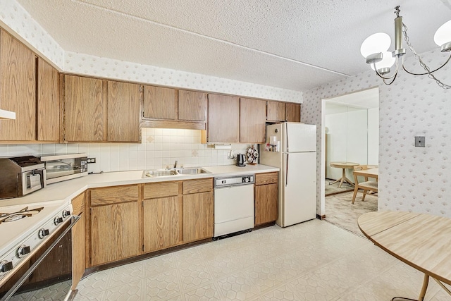 kitchen with wallpapered walls, white appliances, light countertops, a textured ceiling, and a sink