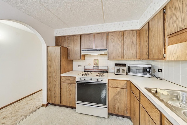 kitchen with under cabinet range hood, a sink, light countertops, white gas range oven, and stainless steel microwave