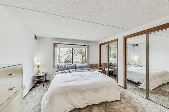 bedroom with two closets, visible vents, light carpet, a textured ceiling, and baseboards