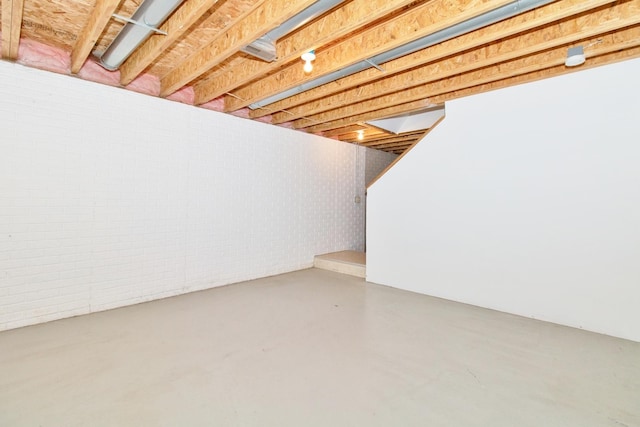 unfinished basement featuring brick wall and stairs