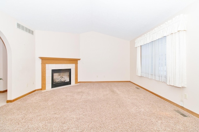 unfurnished living room featuring arched walkways, carpet, a tile fireplace, and visible vents