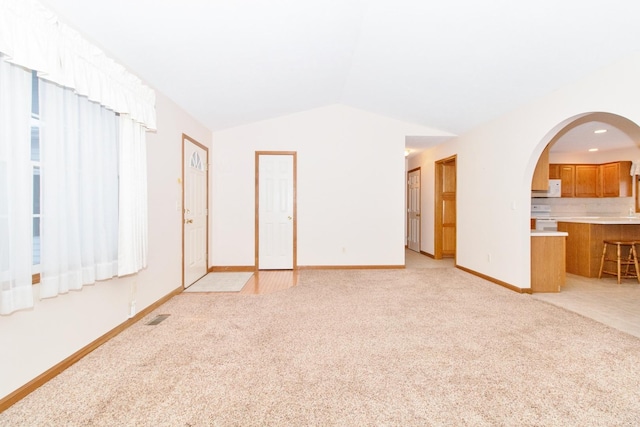 unfurnished living room featuring arched walkways, lofted ceiling, visible vents, light carpet, and baseboards